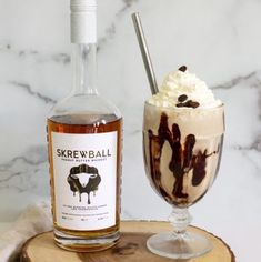 an ice cream sundae next to a bottle of skrew ball syrup on a wooden slice