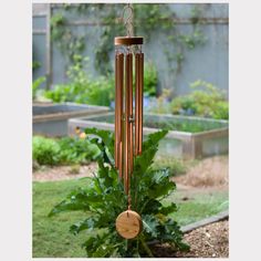 a wind chime hanging from the side of a garden with green plants in the background