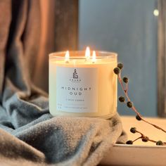 a white candle sitting on top of a window sill next to a gray blanket