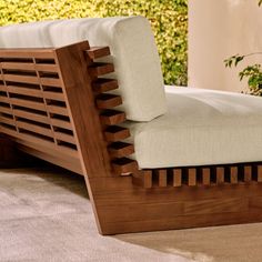 a close up of a wooden bed frame with white sheets on it and plants in the background