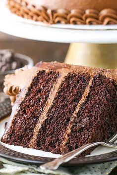 a slice of chocolate cake on a plate with a fork next to it and the rest of the cake in the background