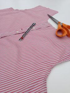 a pair of scissors are sitting on top of a red and white stripped shirt that is being sewn