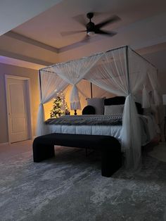 a white canopy bed sitting in a bedroom next to a christmas tree on top of a table