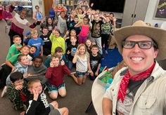 a man wearing a cowboy hat and glasses standing in front of a group of children