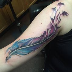 a woman with a tattoo on her arm has a blue and pink feather in it