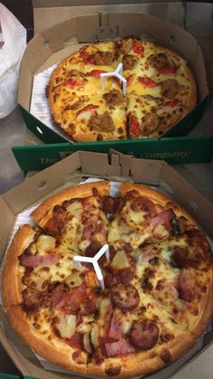 two pizzas with different toppings sitting in boxes