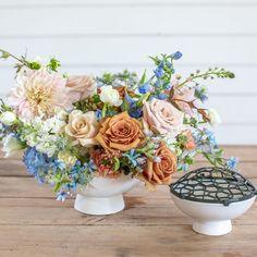 an arrangement of flowers in a white vase on a wooden table next to a birdcage