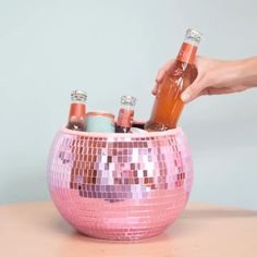 a pink disco ball shaped drink holder with bottles in it and a hand reaching for the bottle