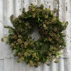 a wreath hanging on the side of a building with green leaves and berries around it