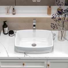 a white bathroom sink sitting on top of a counter next to a vase with flowers