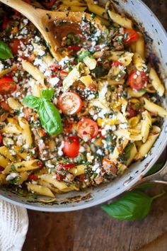 a skillet filled with pasta, spinach and tomatoes on top of a wooden table