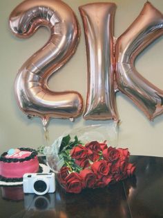 a bouquet of roses sits on a table next to a cake and balloons in the shape of the number twenty