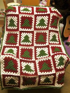 a crocheted blanket with red and green leaves on it, sitting in front of a guitar