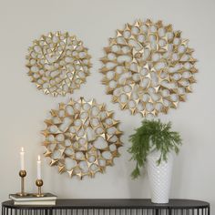 three gold metal wall art pieces on a white wall next to a vase with a green plant