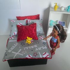 a doll is standing next to a bed with red and gray sheets on it, which has a winnie the pooh pillow