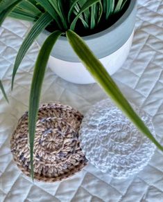 two crocheted baskets sitting on top of a bed next to a potted plant