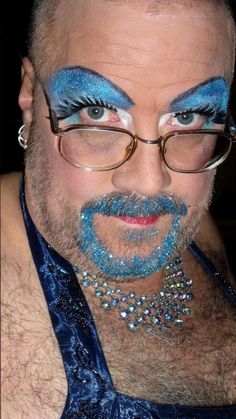 a man with blue makeup on his face and beard, wearing eyeliners and glasses