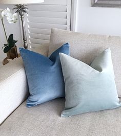 two blue pillows sitting on top of a white couch next to a lamp and window