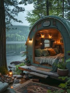 a bed in the middle of a forest next to a body of water with lights on it