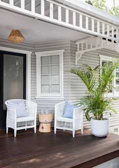 two white wicker chairs sitting on top of a wooden deck next to a potted plant