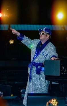 a man in a silver robe and blue hat on stage with his arms out to the side