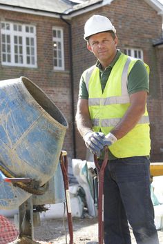 a man in safety vest and hard hat holding a shovel next to a blue barrel