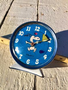 a small blue clock sitting on top of a wooden table next to a fence post