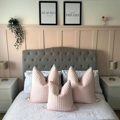 three pink pillows are on top of a gray bed with two framed pictures above it