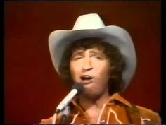 a man wearing a cowboy hat and holding a microphone in front of his face while singing