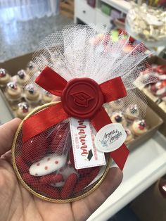 a hand holding a red and white cupcake in a mesh bag with a ribbon around it