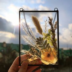 a person holding up a piece of glass with flowers and grass in the sun behind it