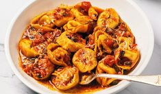 a bowl filled with pasta and sauce on top of a white countertop next to a silver spoon