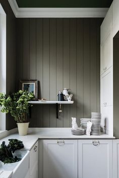 a kitchen with green painted walls and white cupboards filled with dishes, pots and pans