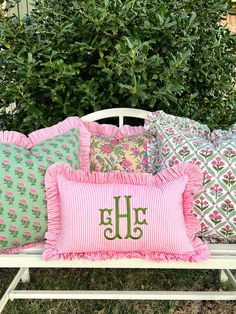 a white bench topped with pillows covered in pink and green pillow cases next to bushes