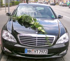 a mercedes benz parked on the side of the road with flowers and greenery attached to it