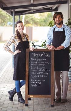 two people standing next to a sign that says menu s and the man is wearing an apron