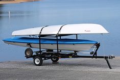 a white and blue boat on trailer next to the water with a surfboard attached to it