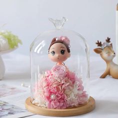 a small doll in a pink dress under a glass clochet with flowers on it