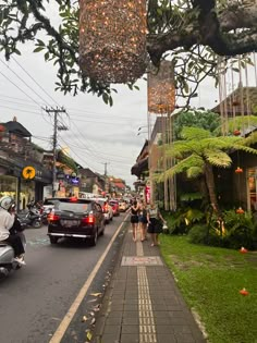 people are walking down the street in front of parked cars and scooters with lights hanging from them