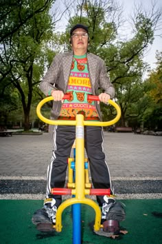 a man riding on the back of a yellow and blue bike next to a park