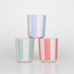 three different colored cups sitting next to each other on a white surface with no one around them