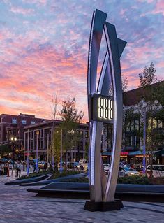 a large metal sculpture sitting in the middle of a city square at sunset with people walking around