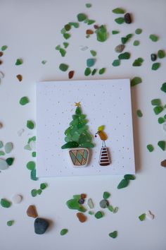 a card with a christmas tree on it and green sea glass scattered around the card