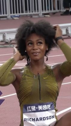 a woman sitting on top of a race track holding her hair in one hand and smiling at the camera