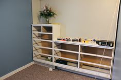 a white shelf with some flowers and other items on it next to a blue wall