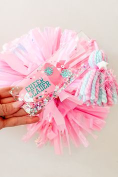 a hand holding a pink and blue cheerleader pom - pom