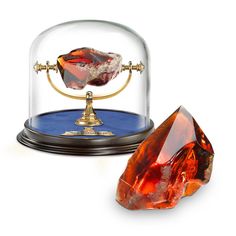 an orange diamond under a glass dome on a blue base with a gold stand underneath it