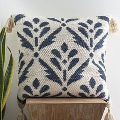 a blue and white pillow sitting on top of a wooden shelf next to a potted plant