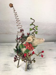 a white teddy bear sitting on top of a table next to a wire sculpture with red berries and greenery