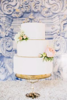 a three tiered white wedding cake with pink flowers on the top and gold trim